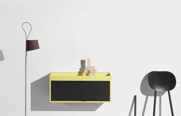 Minimalist room with yellow cabinet, modern floor lamp, and black chair casting shadows.